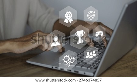Gamification concept in learning, interactive engaging content displayed through digital hexagonal icons like trophies, medals, and targets as a person types on a laptop. This image illustrates the integration of game mechanics into non-game environments to increase user retention, motivation, and productivity. It highlights the modern approach to corporate training, e-learning platforms, and strategic business development where progress is tracked through rewards. The visual focus is on the seamless blend of technology and human interaction, showcasing how digital tools can transform a standard workflow into an immersive, achievement-oriented experience