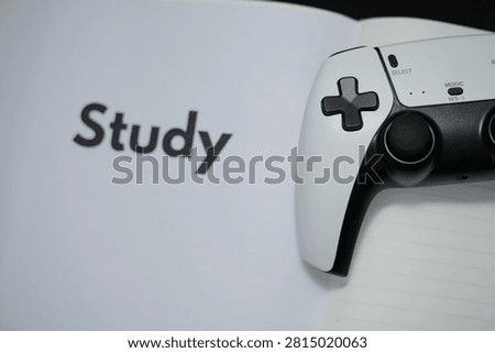 A gaming controller rests on an open notebook with the word study. The scene suggests a blend of gaming and studying together in modern life.