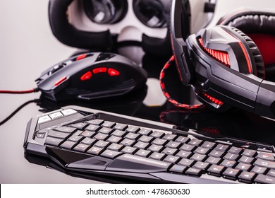 A Gaming Keyboard, Mouse, Headset And Virtual Reality Glasses Shot Over A Dark Reflective Surface