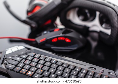 A Gaming Keyboard, Mouse, Headset And Virtual Reality Glasses Shot Over A Dark Reflective Surface