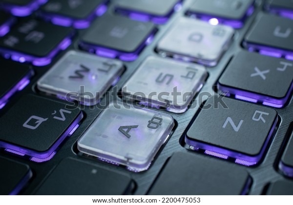 Gaming\
laptop keyboard with Latin and Cyrillic fonts. Purple backlight\
keys. Fragment with the semitransparent WASD\
keys.
