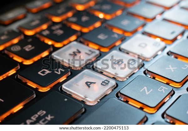Gaming laptop keyboard with Latin and Cyrillic\
fonts. Bright orange backlight keys. Fragment with the\
semitransparent WASD\
keys.