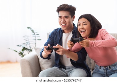 Gaming Together. Excited Asian Couple Playing Videogames Sitting On Couch At Home, Having Fun On Weekend. Computer Gaming, Video Games For Family Of Two, Weekend Leisure Concept