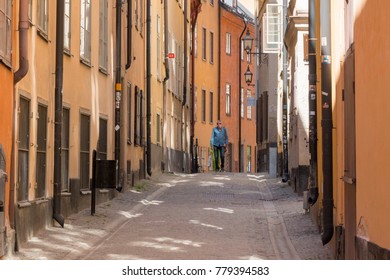 Gamla Stan, Stockholm, Sweden; July 23, 2016; Cobbled Street With Townhouses Each Side.  Middle Aged Man In Distance Walking Towards Camera. Light From Windows Reflected On Ground.