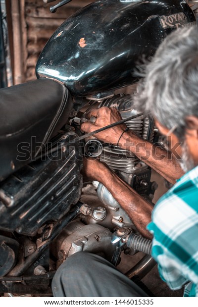 Gangavathi / India -\
July 8 2019: A mechanic in a small workshop repairing the\
carburettor on an old\
motorcycle.