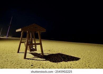 Gangneung, South Korea - November 3rd, 2024: A solitary wooden swing sits on the sandy shores of Gyeongpodae Beach under the night sky, casting a shadow in the dim light. - Powered by Shutterstock