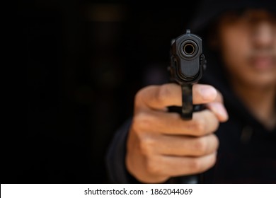 The gangster aimed a gun at the camera. A thief pointing a gun at the target on dark background. selective focus on front gun, Blurred focus.