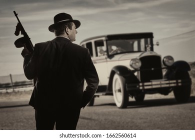 Gangster standing on a road, with a vintage car in the background