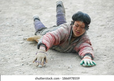 Gansu, China. Feb 27, 2007. A Tibetan Buddhist pilgrim does full body prostrations. He is kneeling down, sliding the forearms along the road. His face covered with mud.
