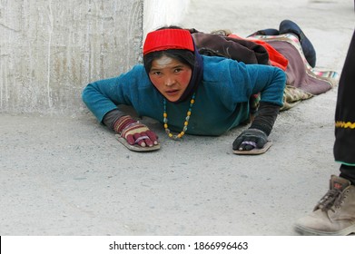 Gansu, China. Feb 27, 2007. Chinese female pilgrim in traditional costumes does full body prostrations. She kneeling down on the ground with arms reaching out. Tibetan Buddhism practice.