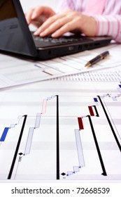 Gantt Chart With Project Manager Working On Laptop In Background. Selective Focus On Foreground.