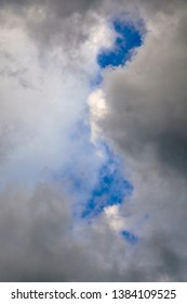 Gaps In Shadowy Clouds Reveal Blue Sky On A Summer Evening, For Background Or Element With Themes Of Coming Into Sight And Brief Looks