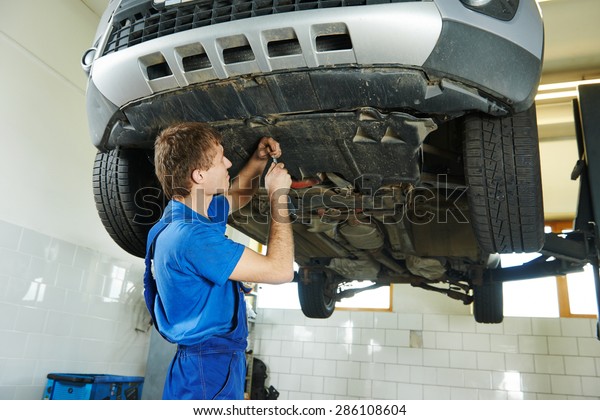 garage auto mechanic repairman assembling bottom\
car protection during car suspension repair of automobile\
maintenance at repair service\
station