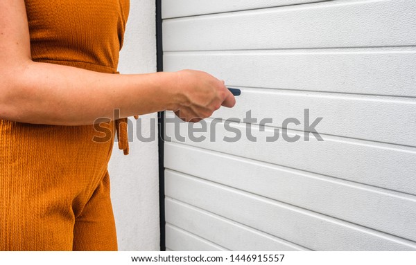  Garage door PVC. Girl or\
young woman holds remote controller for closing and opening garage\
door
