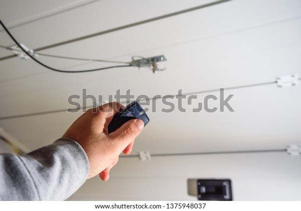 Garage door PVC. Hand uses remote controller\
for closing and opening garage\
door