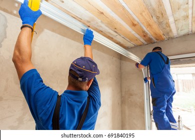 Garage Doors Installation. Workers Installing  Post Rail And Spring Installation / Assembly.