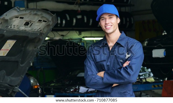 In a garage, a mechanic after having checked\
and checked the oil and engine at the car smiles because the car\
has been repaired successfully. Concept of: security,safety,\
insurance and assistance
