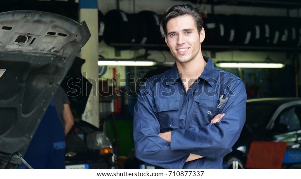In a garage, a mechanic after having checked\
and checked the oil and engine at the car smiles because the car\
has been repaired successfully. Concept of: security,safety,\
insurance and assistance