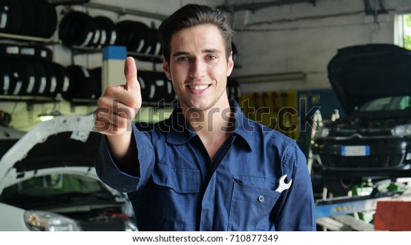 In\
a garage a mechanic after having checked and done the machine makes\
ok with his thumb up and smiles because the car has been repaired\
successfully. Concept of: security, safety,\
insurance.