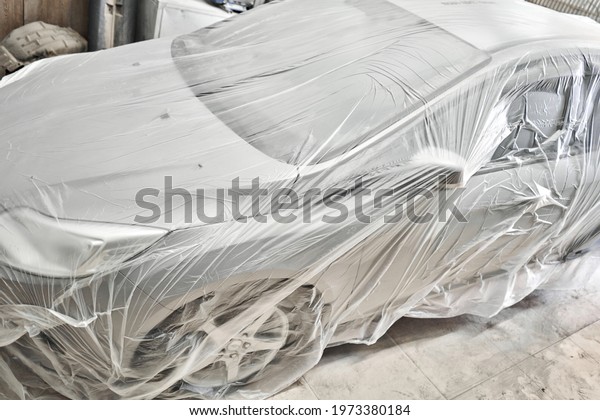 Garage painting car service. section of the car\
is covered with primer. vehicle is covered with protective paper.\
Repairing car body work after the accident by working sanding\
primer before painting.