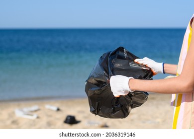 Garbage Bag In Hands Against The Background Of A Dirty Seashore. The Concept Of Preparing For The Collection Of Garbage On The Beach. Selective Focusing.