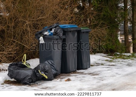 Garbage bin full of trash on white snow in residential area in winter.