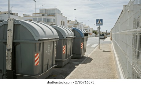 Garbage bins sharp in foreground with shallow defocused background on a sunlit sidewalk street; background backdrop copyspace calm.