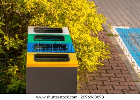 Garbage cans in different colors - selective waste collection in the tiny city square. Four waste bins in a row feature color-coded lids in white, green, blue, and yellow, indicating selective waste 