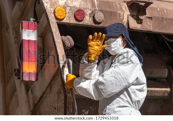 Garbage man in respiratory mask\
collects rubbish to garbage car in Cusco, Peru during coronavirus\
pandemic in Latin South America. Epidemic of coronavirus\
covid-19