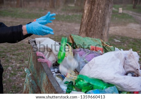 garbage in the nature, cleaning the environment in the spring on the river from the rubbish a woman in disposable latex blue mittens in to blue large plastic bag