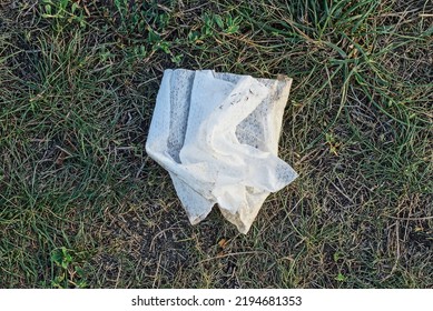 Garbage From One White Dirty Crumpled Paper Napkin Lies On Gray Ground And Green Grass In Nature