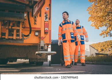 Garbage Removal Men Working For A Public Utility Emptying Trash Container