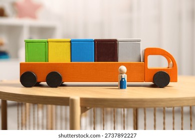 Garbage sorting play set for children. Toy truck with bright trash bins and human figure on wooden table indoors, closeup