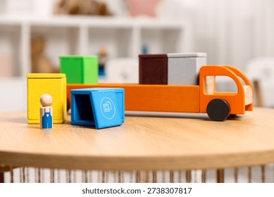 Garbage sorting play set for children. Toy truck, bright trash bins and human figure on wooden table indoors, closeup