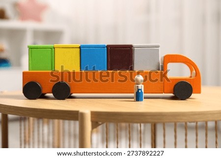 Garbage sorting play set for children. Toy truck with bright trash bins and human figure on wooden table indoors, closeup