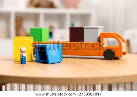 Garbage sorting play set for children. Toy truck, bright trash bins and human figure on wooden table indoors, closeup