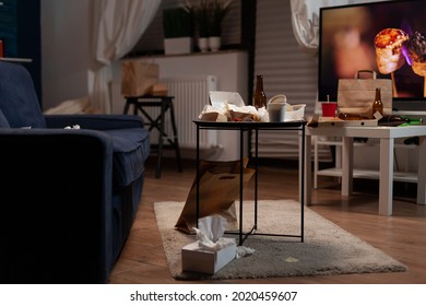 Garbage table with empty beer drink bottle and food rubbish placed in living room of lonely person. Unorganized house of alone person with sever depresion having trash, rubbish, napkins on sofa