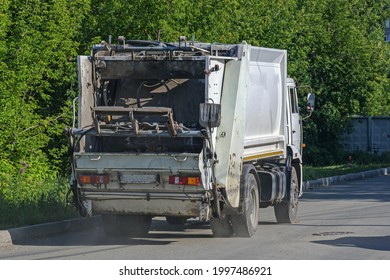 A Garbage Truck Is Driving Down The Street On A Summer Day