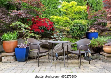 Garden backyard with lush plants landscaping and stone paver patio hardscape with wicker bistro furniture chair and table set in spring season - Powered by Shutterstock