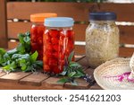 Garden cart wood counter and mason jars with fermenting cherry tomatoes and cabbage, surrounded by fresh basil and thai basil leave and straw hat