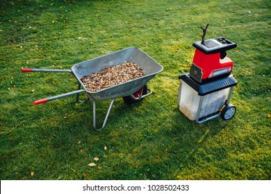 garden chipper, electric shredder (mulcher) with wheelbarrow full of wooden mulch, green grass background - Shutterstock ID 1028502433