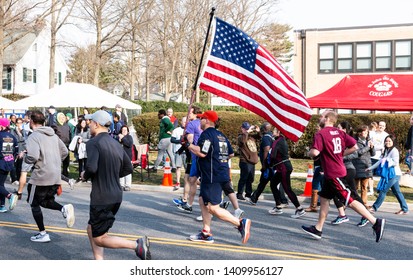 Garden City, New York, USA - 30 March 2019: A Runner Is Carrying An American Flag During A 5K Charity Road Race.