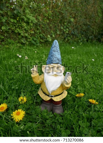 Garden dwarf with mobile phone on a green meadow makes a selfi with peace sign

