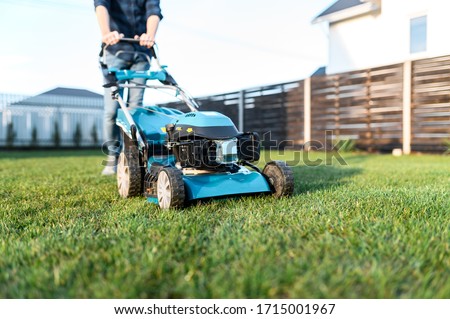 Garden equipment. Gas-push lawn mower on the green grass, male legs on background