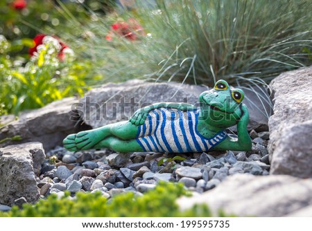 Garden frog lying among beautiful flowers, artificial toy