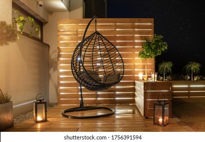 Garden Furniture Design. Starry Night Time In Stylish Backyard Garden With Wooden Porch With Wall And Planters Illuminated By Modern LED Lighting.