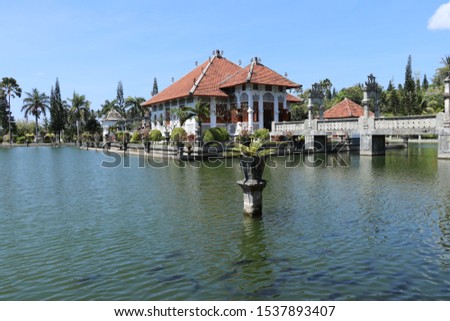 Garden gazebo in the garden above the water surface. White Balinese style house with ornamental columns and ocher roof. The Stone Bridge is an access road to an architectural gem. Tropical vegetation.