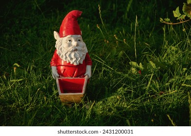 Garden gnome ornament figurine in red with wheelbarrow. Gardener working at the garden.
