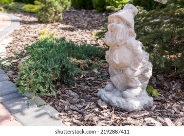 A Garden Gnome In Sunny Weather Stands On A Plot On The Grass. Garden Gnome As An Element Of Landscape Design, With A Soft Blurred Background	
