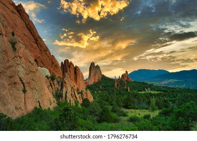 Garden Of The Gods With Colorful Sunset. Beautiful Colors Cast Light On The Rock Formations In Colorado Springs. Colorful Clouds, Green Trees, And Orange Rocks Visible